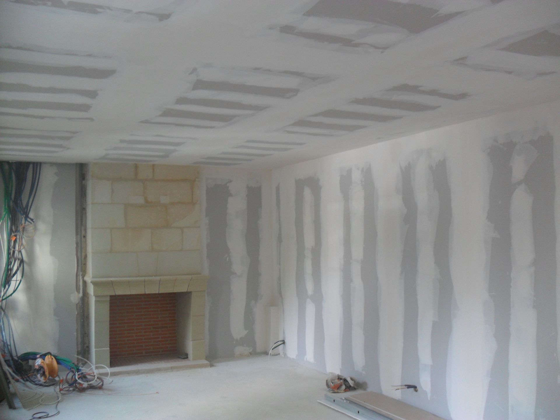 Pièce intérieure en travaux, poutres apparentes au plafond et cloisons sèches. Cheminée.