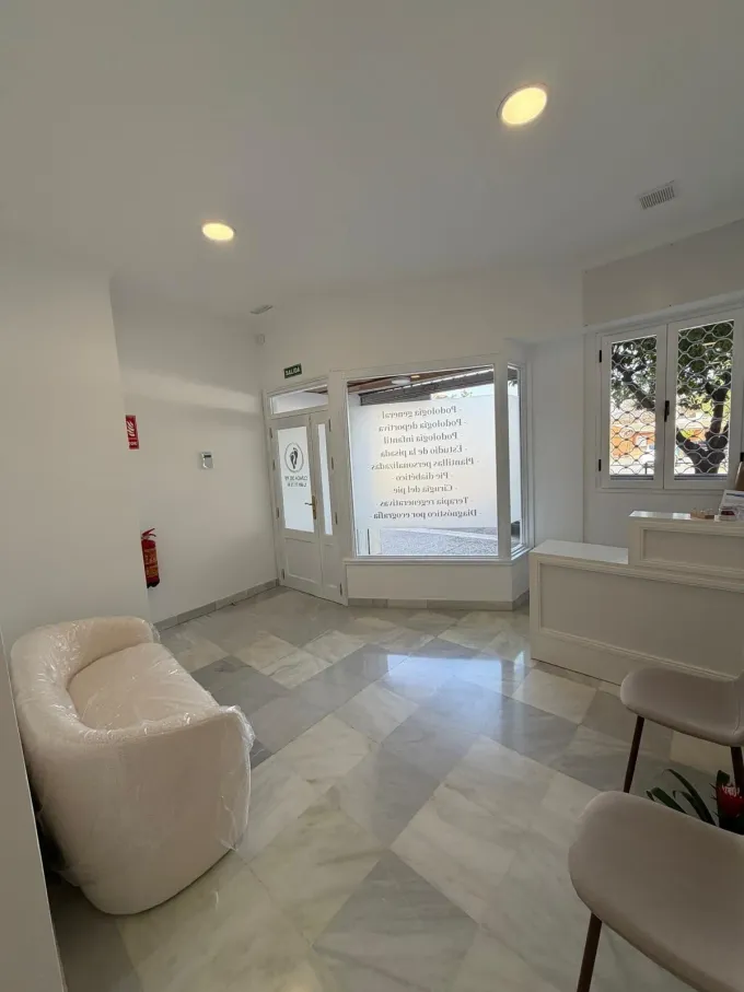 Vestíbulo blanco luminoso con asientos curvos, suelo de mármol, luces empotradas y puertas de entrada de cristal.