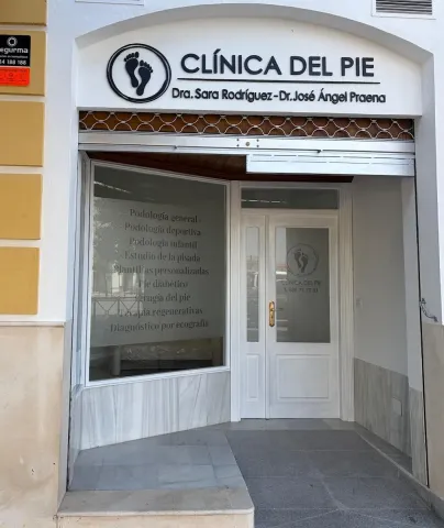 Entrada de la clínica con letrero blanco que dice “CLINICA DEL PIE”, puerta de cristal y escaparate.