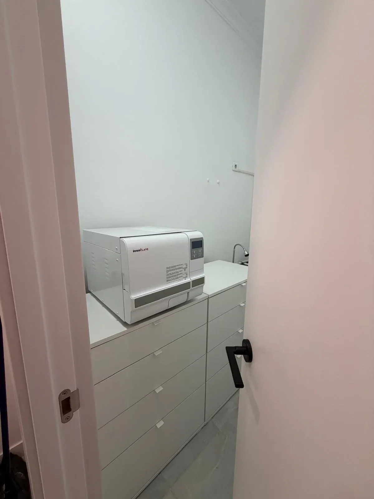 Una pequeña impresora blanca sobre una cómoda en un pasillo estrecho, vista a través de una puerta abierta.