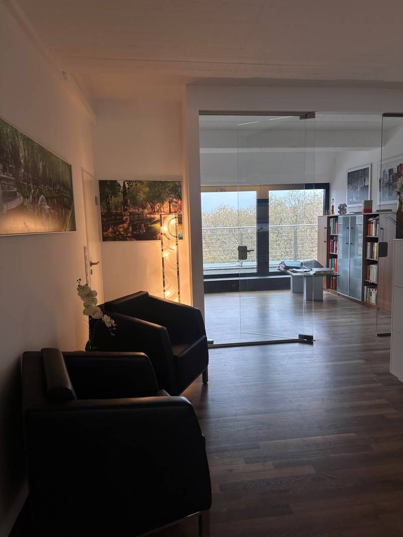 Modernes Wohnzimmer mit dunklen Stühlen, Holzboden, Wandkunst und großen Fenstern mit Blick auf eine helle Aussicht