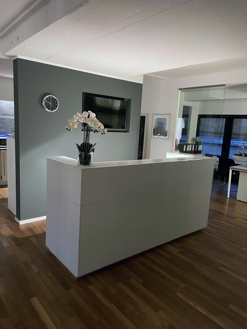 Modernes Wohnzimmer mit weißem Empfangstresen, wandmontiertem Fernseher und Blumen vor einer grauen Akzentwand