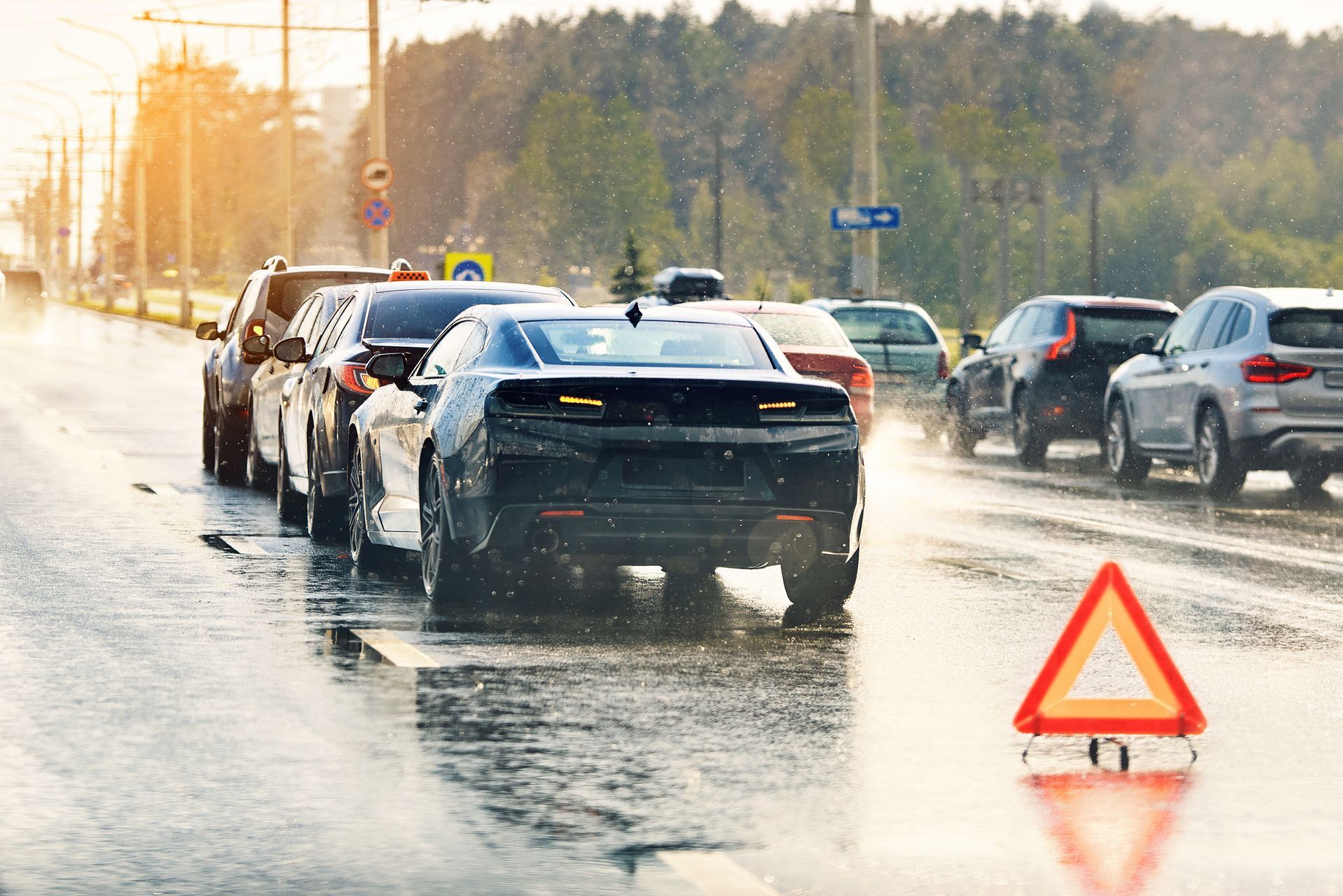 Verkehrsstau auf einer nassen Straße, im Vordergrund ein Warndreieck.