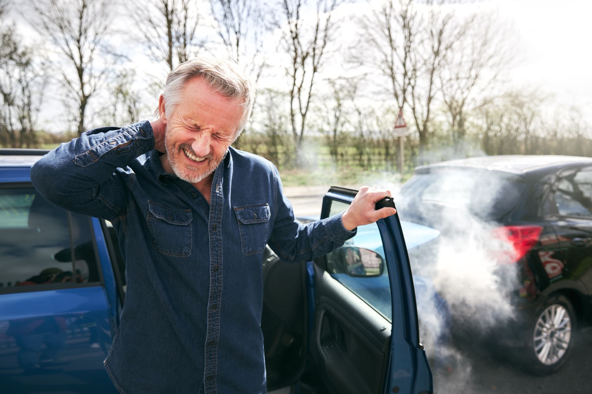 Ein Mann öffnet auf einem Parkplatz die Autotür und steigt aus. In der Nähe ist sichtbarer Auspuffrauch oder Dampf zu sehen.