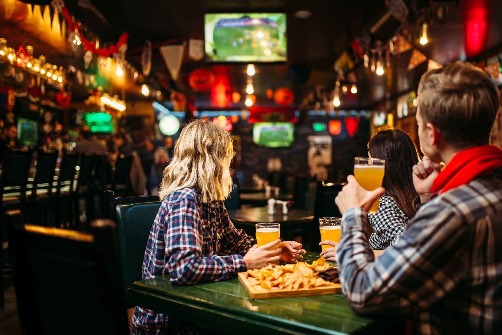 Des gens assis dans un bar, devant un écran, buvant de la bière.