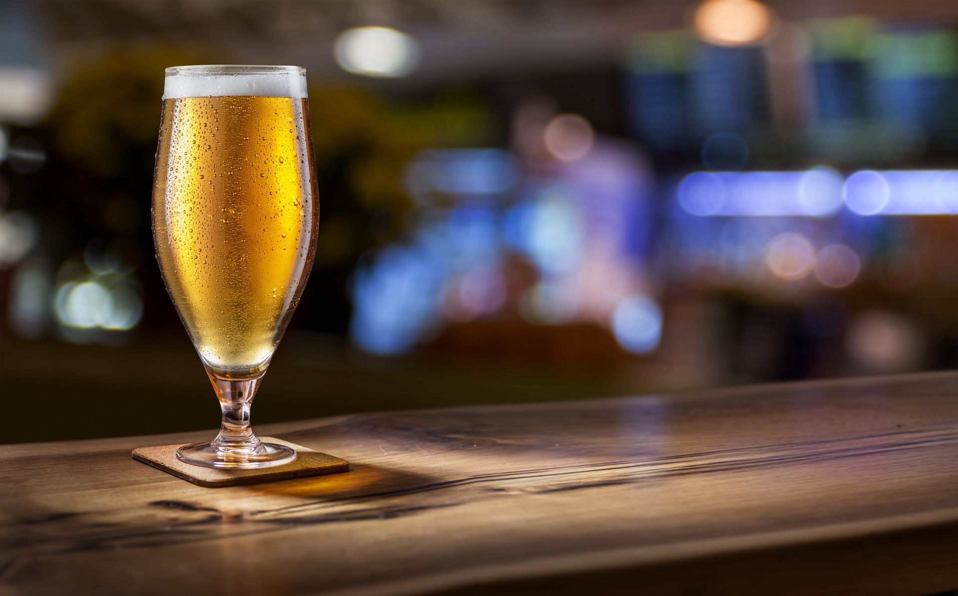 Verre de bière fraîche sur un bar en bois avec un arrière-plan flou d'un pub.