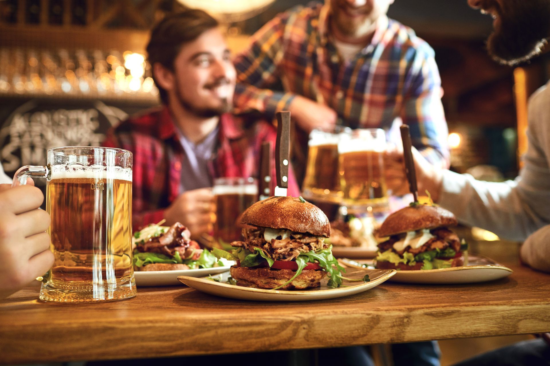 Des amis au pub, mangeant des hamburgers et buvant de la bière. Table en bois, expressions joyeuses, lumière chaleureuse.