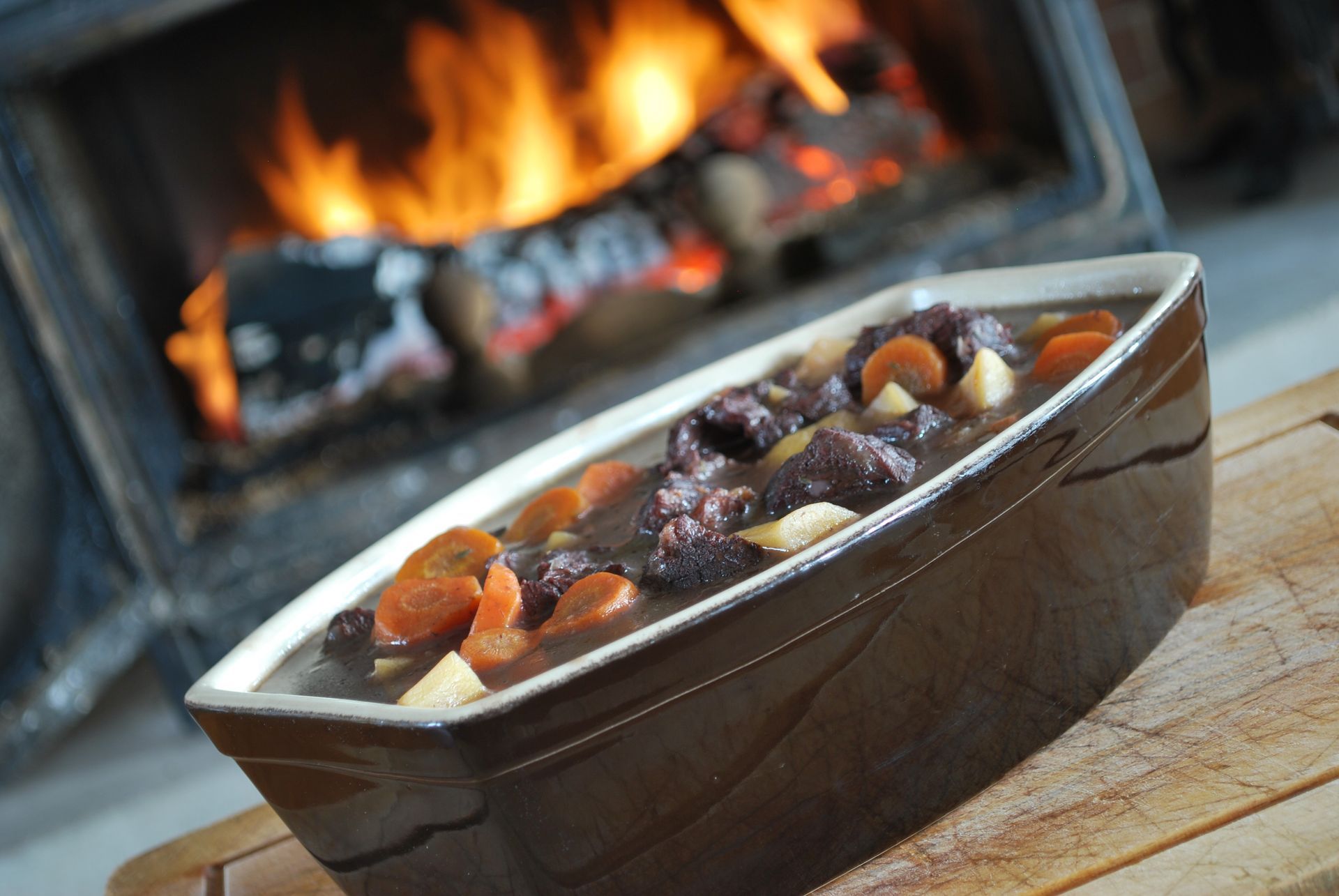Ragoût de bœuf dans un plat brun, avec des carottes, à côté d'une cheminée.