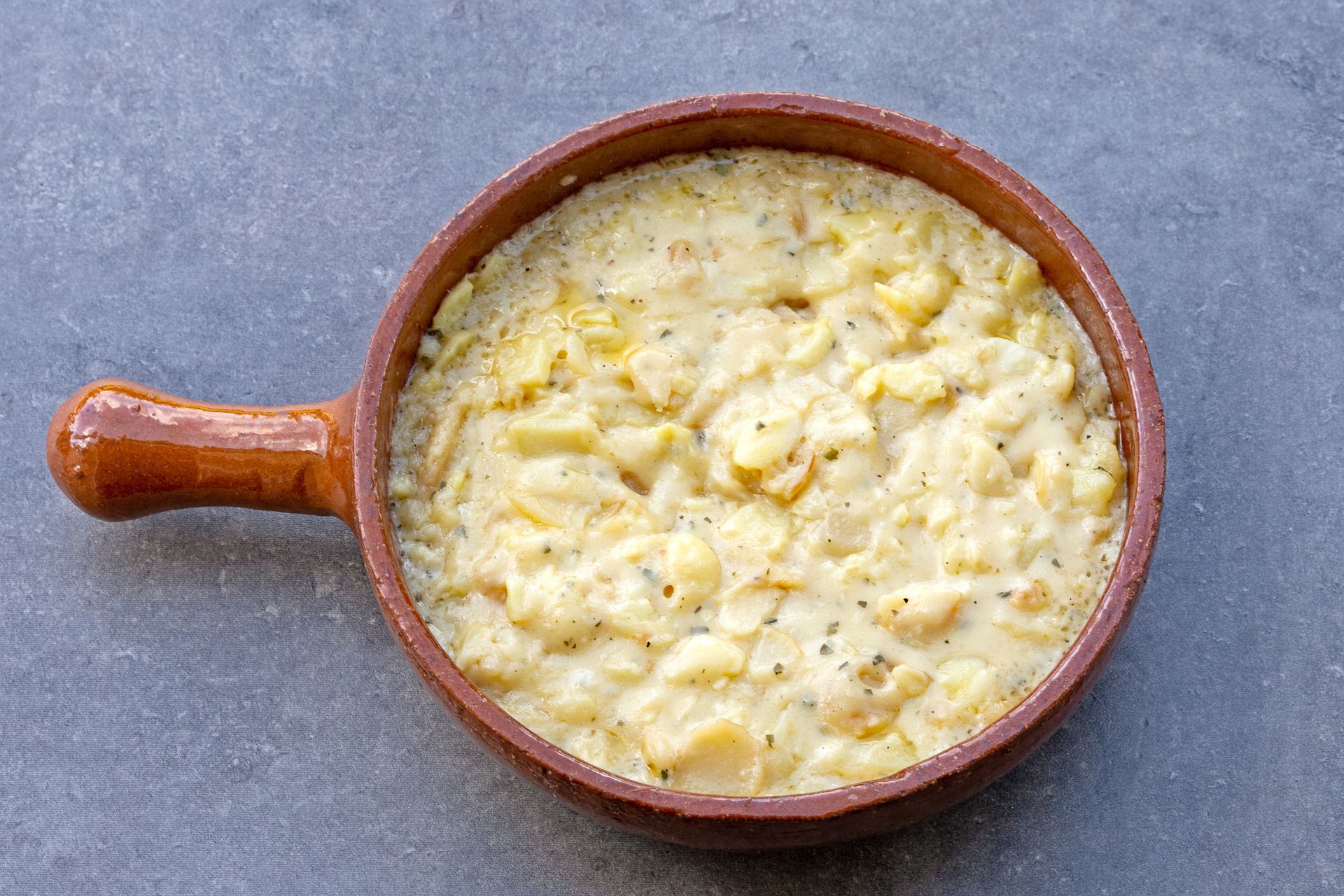 Plat de pommes de terre crémeux dans un plat de cuisson en céramique marron sur une surface grise.