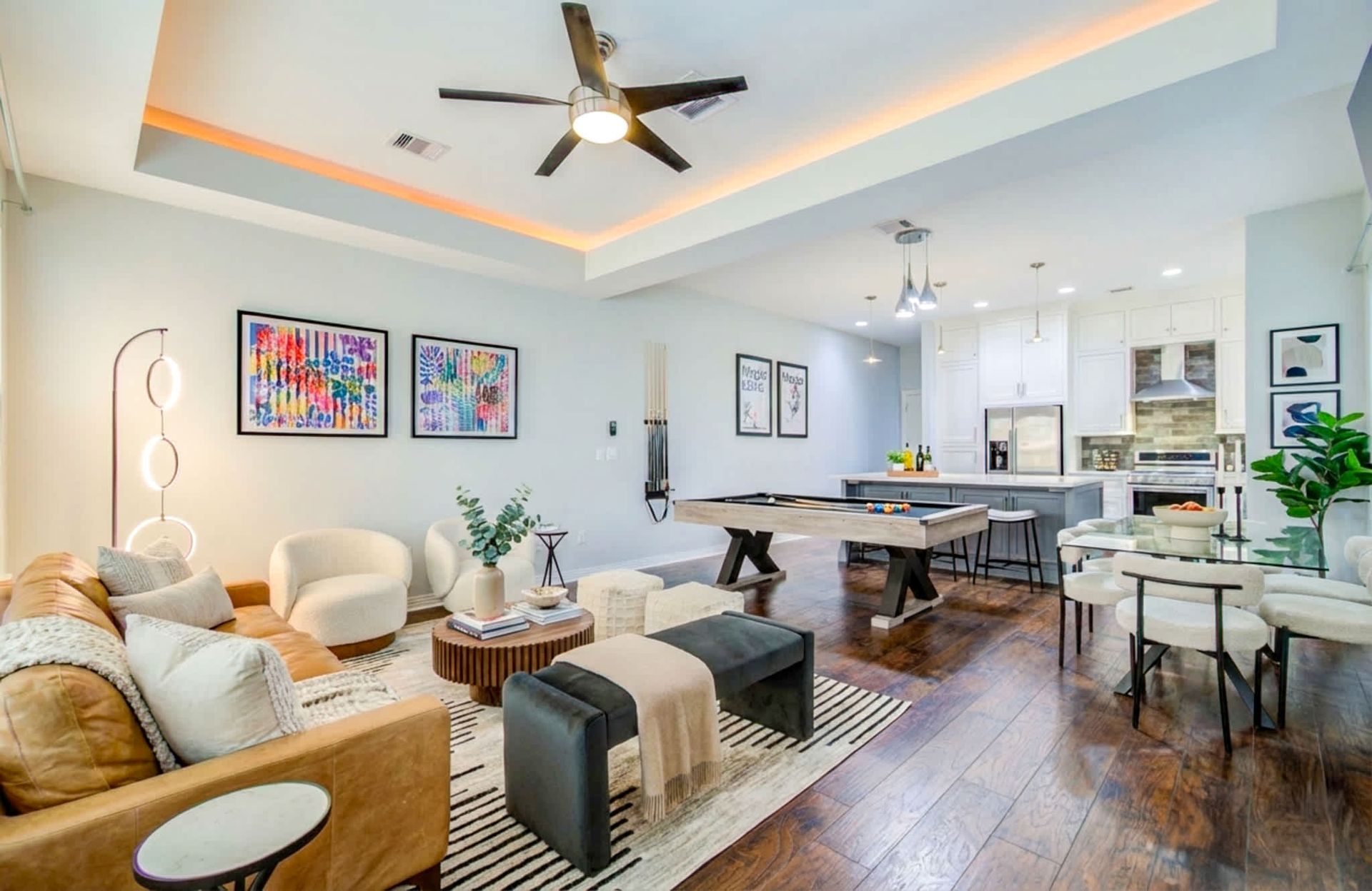 Bright modern living room and dining area with white chairs, gray sofa, artwork, and a ceiling fan