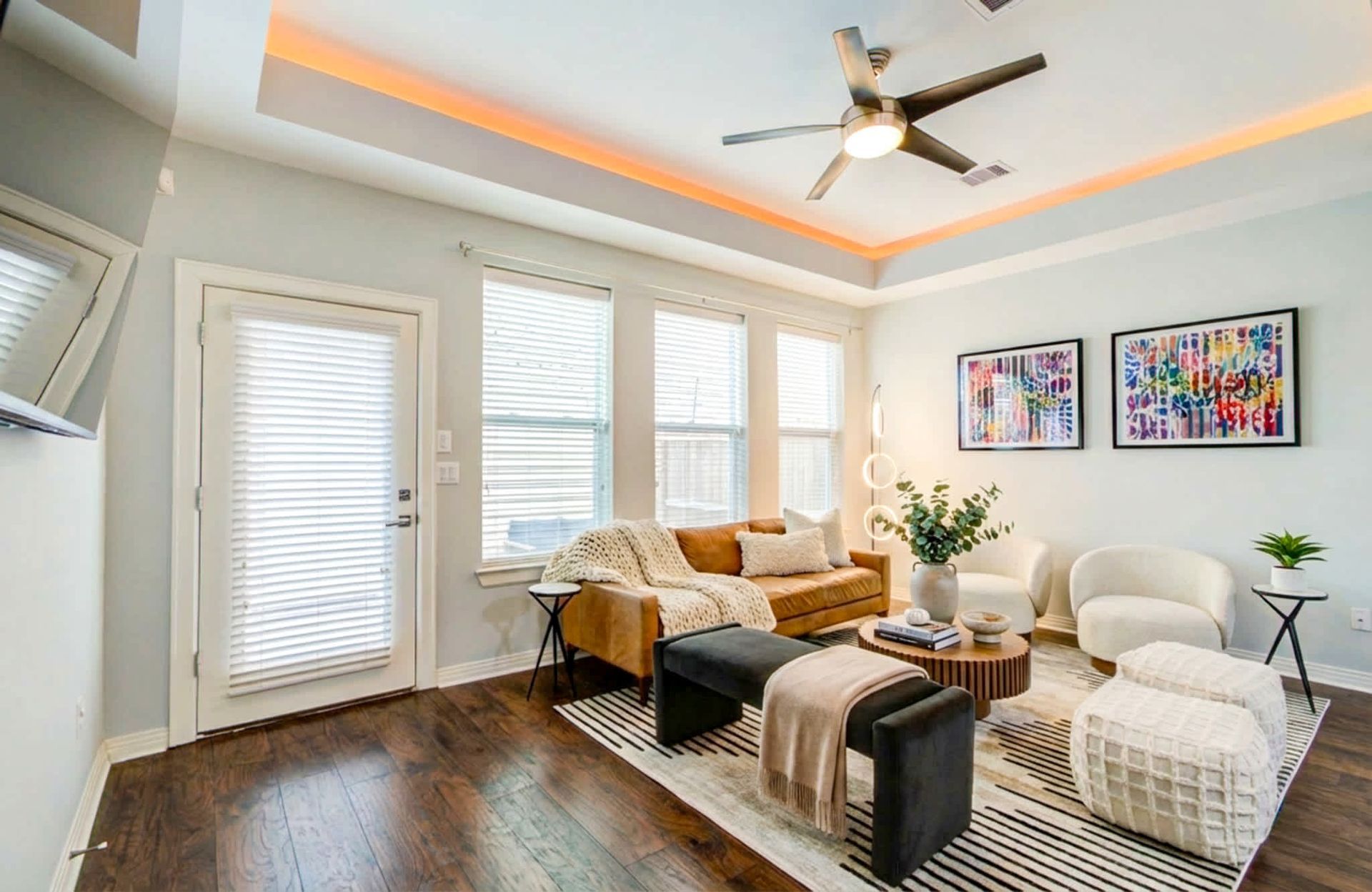 Bright modern living room with white chairs, sofa, ceiling fan, and framed art.