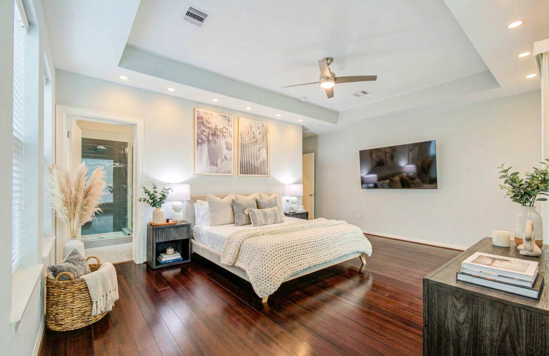 Bright modern bedroom with a large bed, dark wood floors, wall-mounted TV, and vaulted ceiling