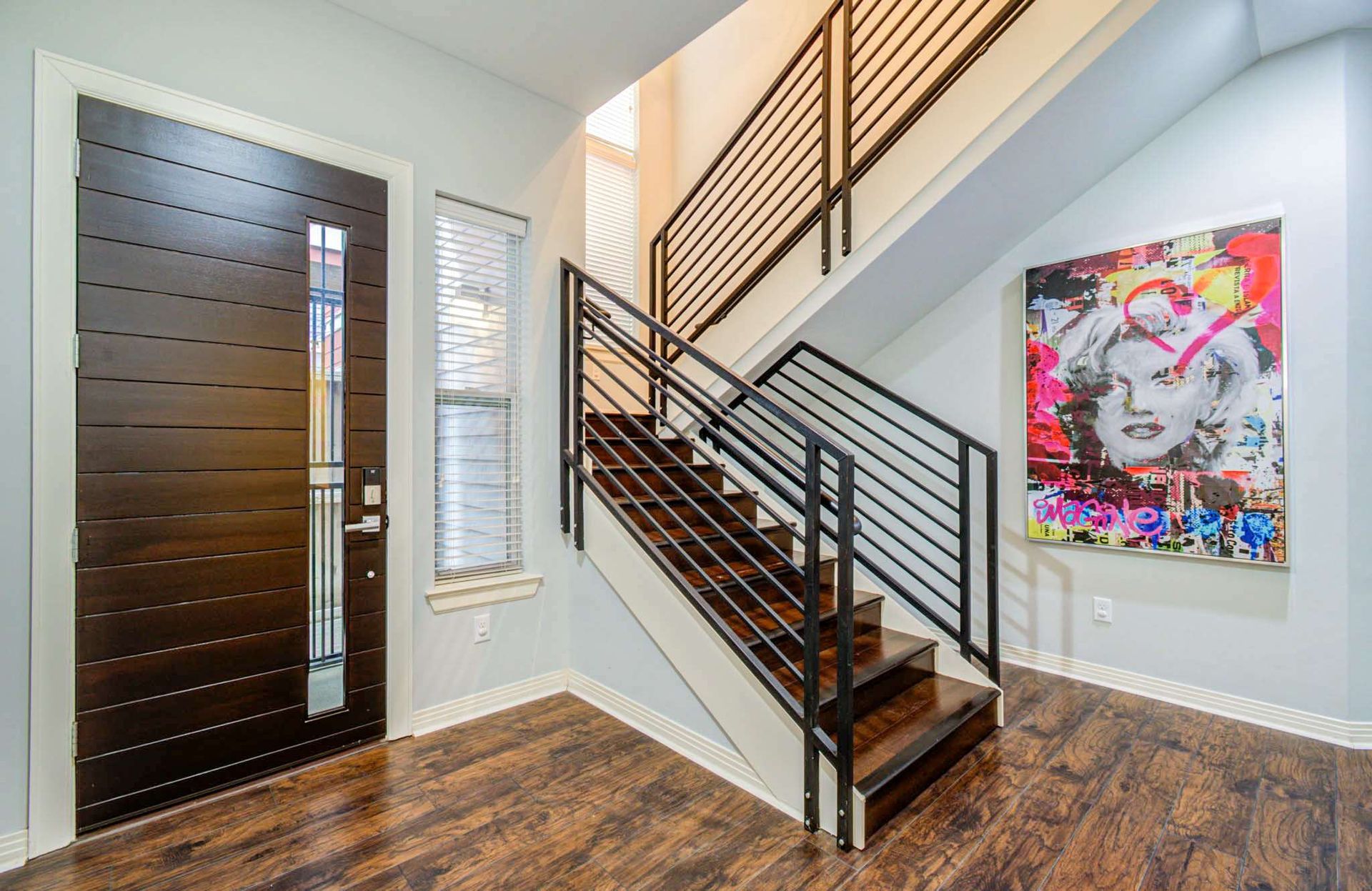 Modern foyer with dark front door, staircase, wood floors, and colorful wall art