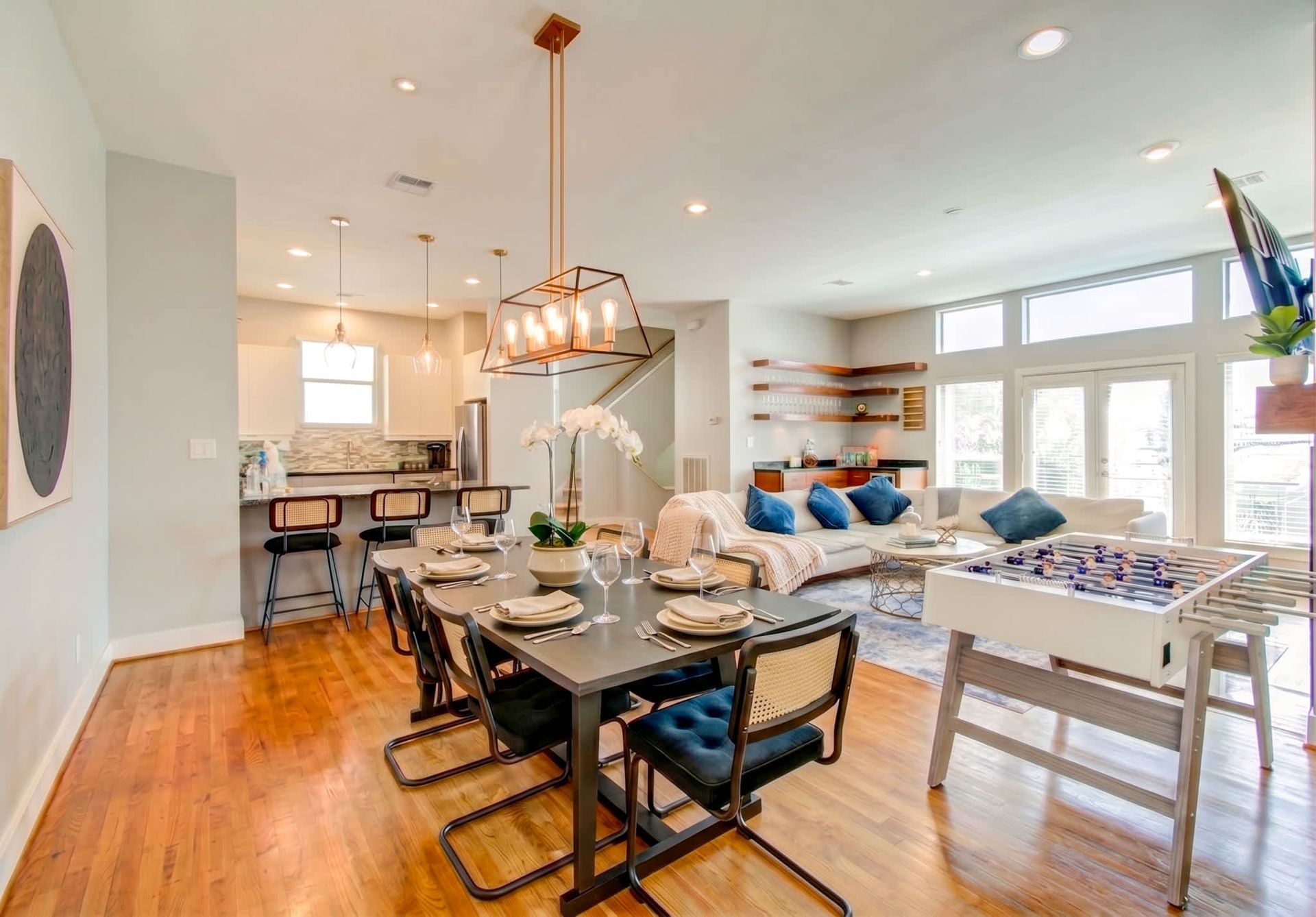 Open dining and living room with hardwood floors, modern table, blue sofa, and bright windows