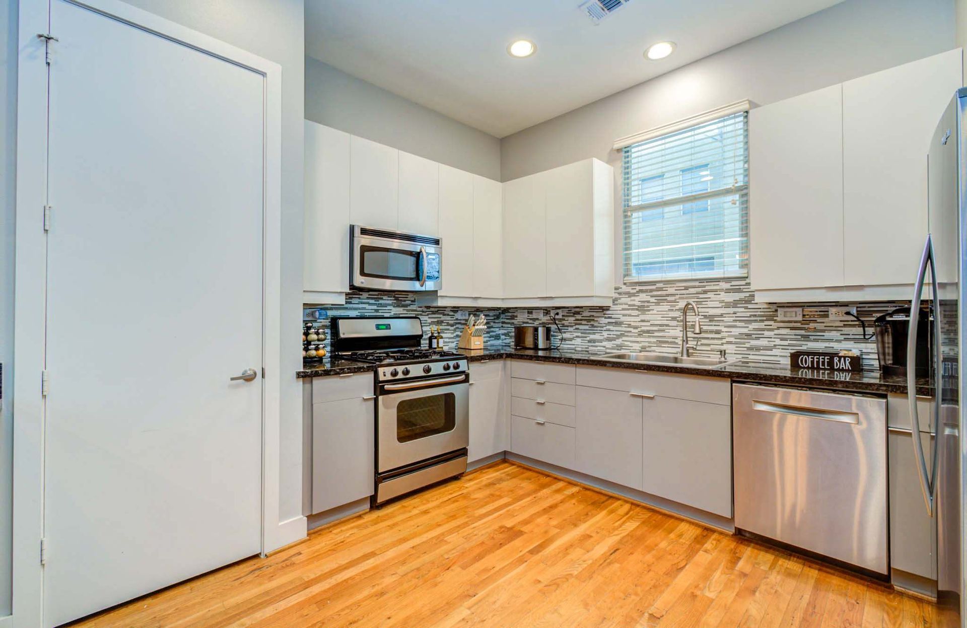 Modern kitchen with white cabinets, stainless steel appliances, tiled backsplash, and hardwood floors