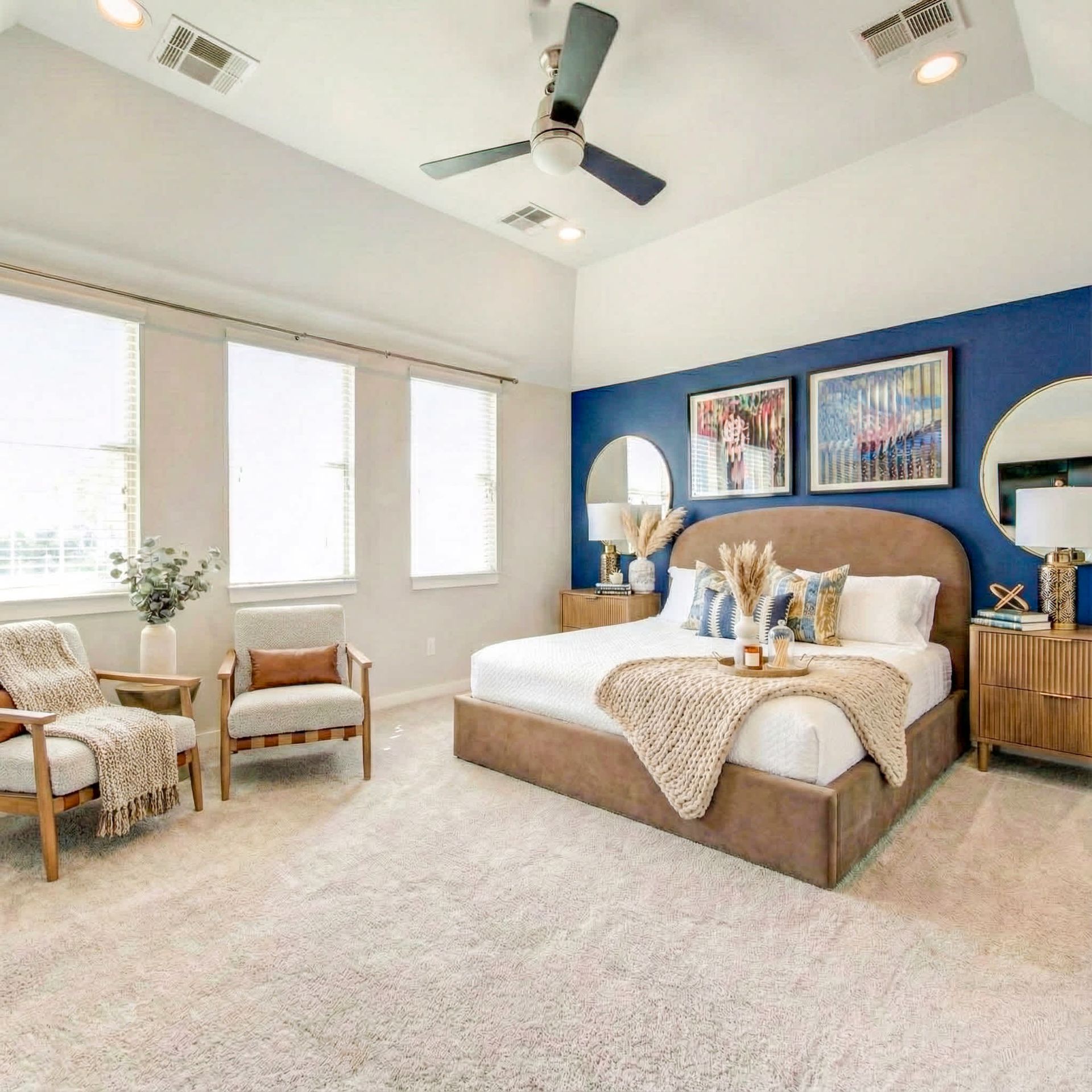 Bright bedroom with a blue accent wall, king bed, beige chairs, and large windows.