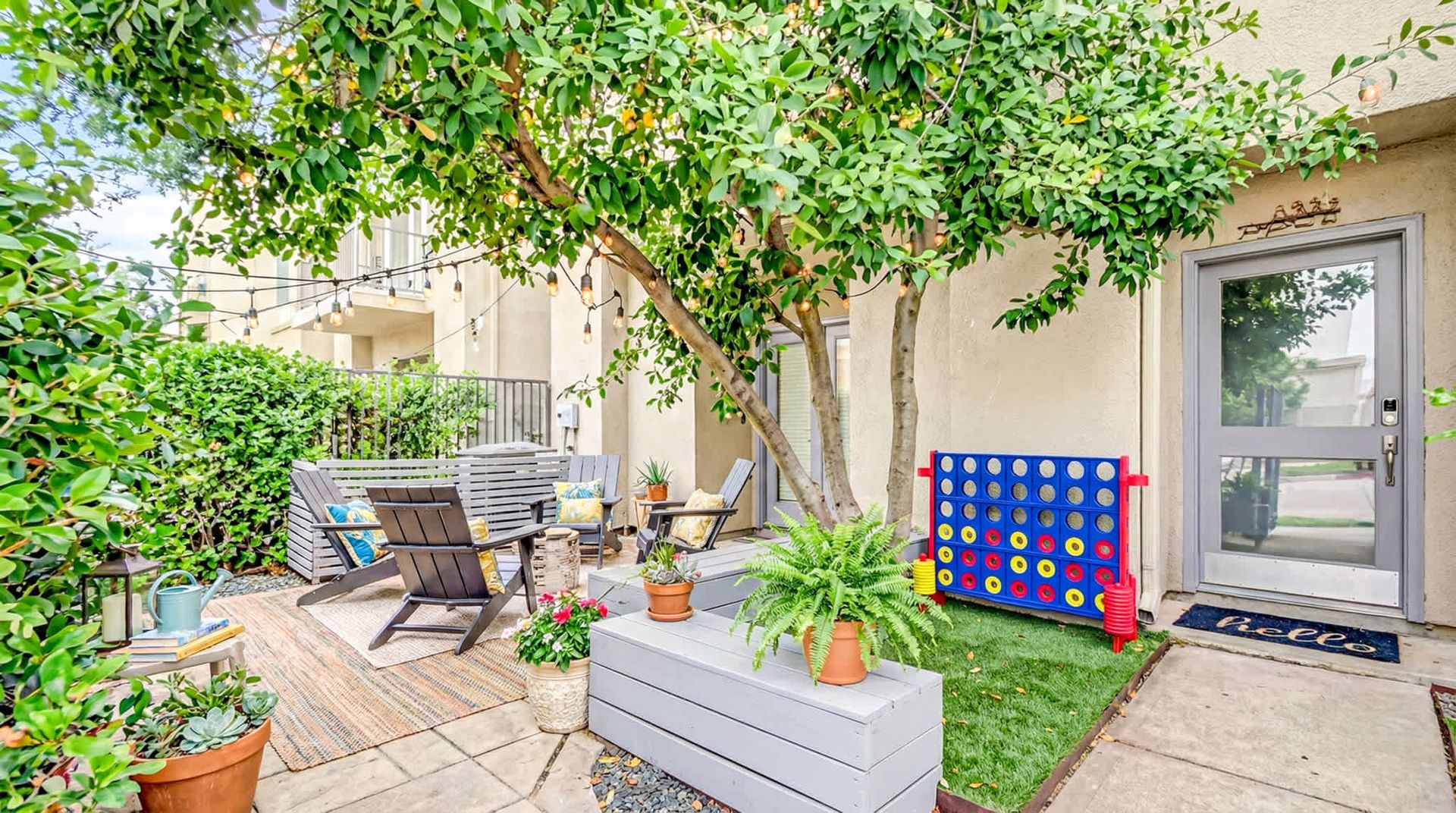 Patio with outdoor dining set, potted plants, tree shade, and a colorful Connect Four game board