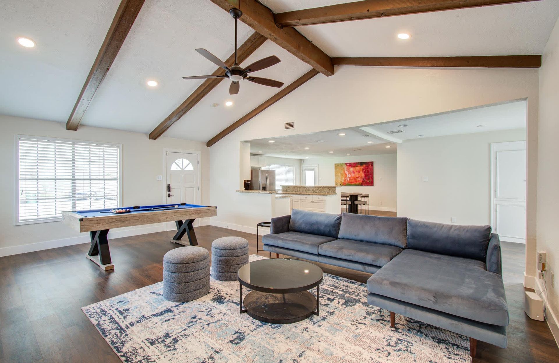 Bright open living room with exposed beams, gray sectional, pool table, and patterned rug