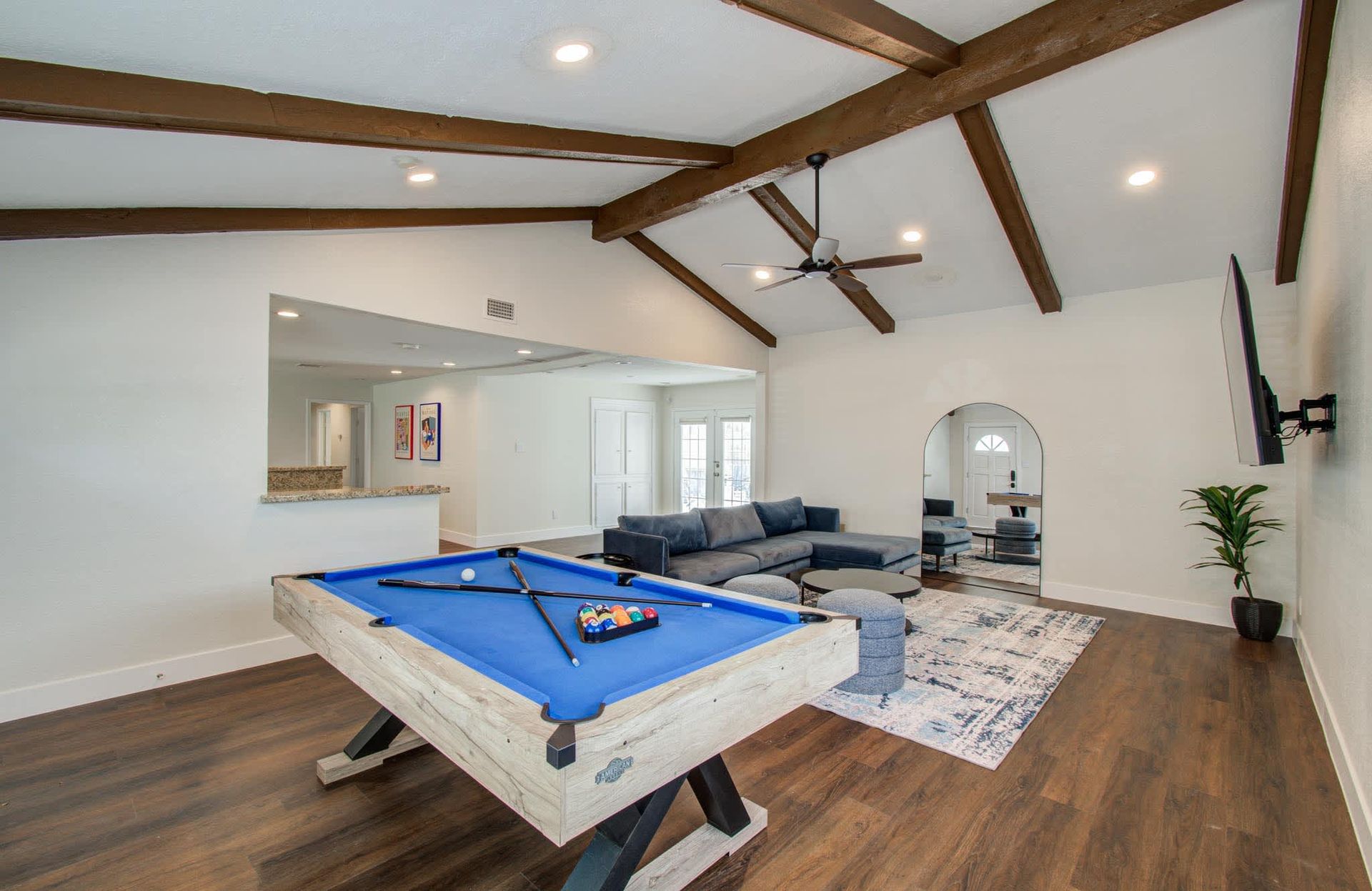 Game room with a blue pool table, sectional sofa, wall-mounted TV, and wood-beamed ceiling