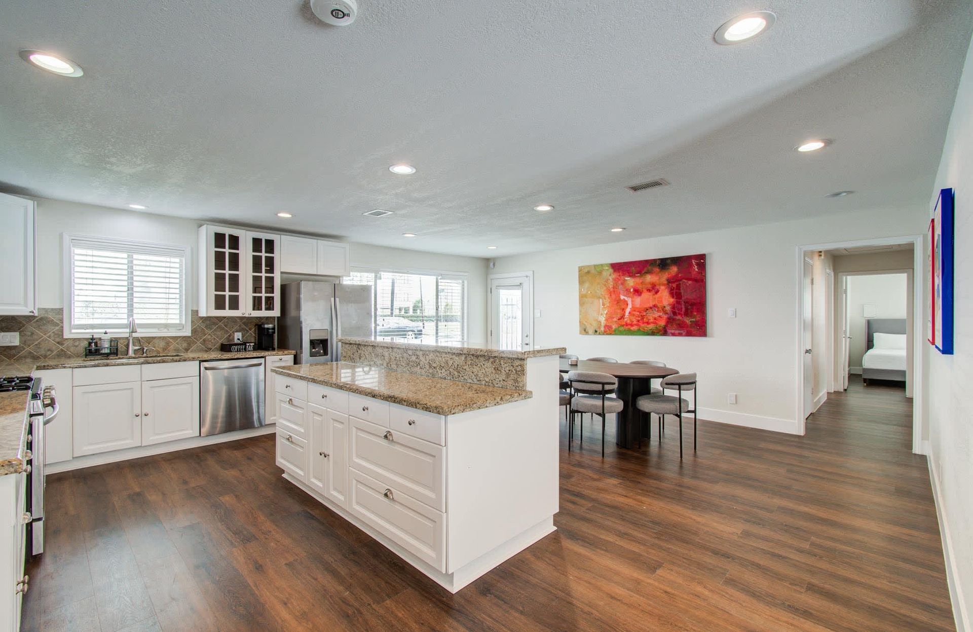 Bright modern kitchen with white cabinets, granite island, wood floors, and dining area by colorful wall art