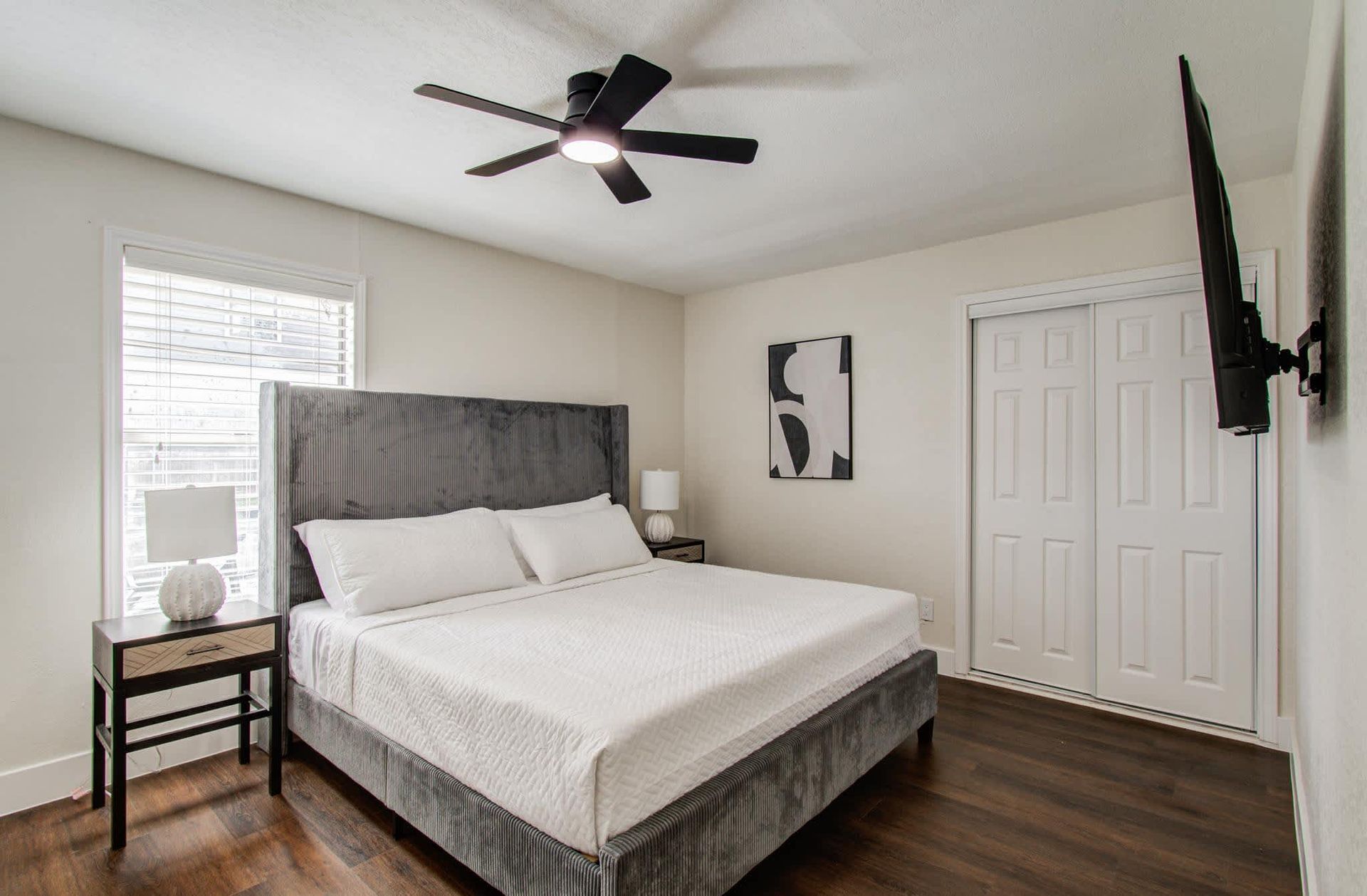 Bright modern bedroom with a bed, nightstands, ceiling fan, and wall-mounted TV