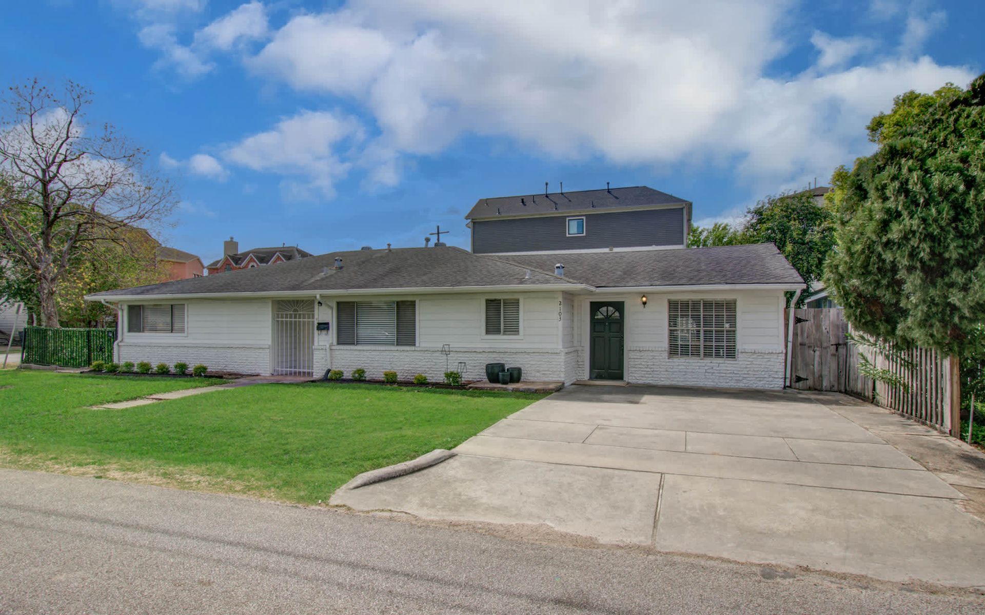Single-story white house with a driveway, green lawn, and blue sky with clouds