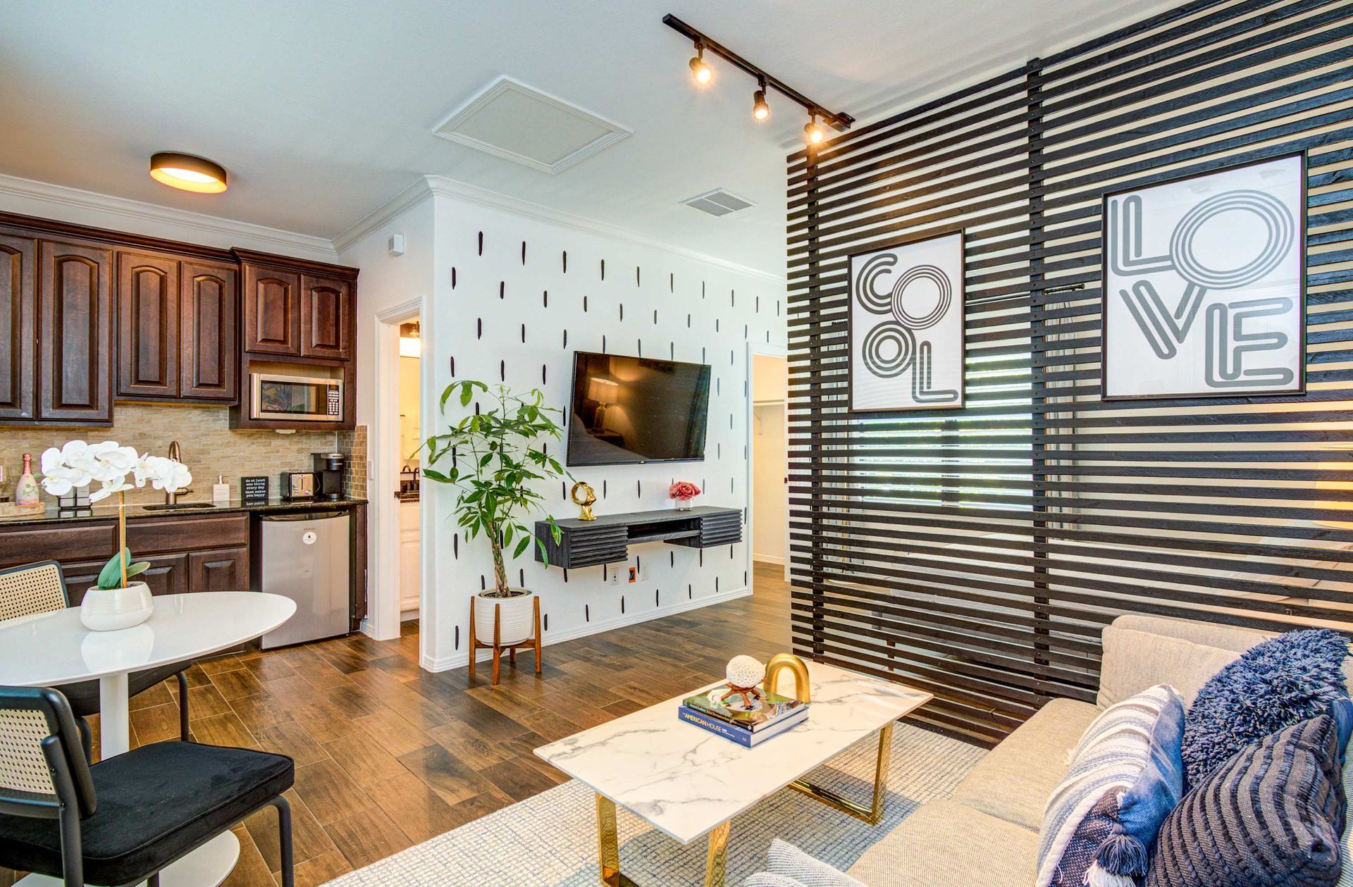 Open-plan living room and kitchen with TV, coffee table, striped accent wall, and “LOVE” art prints