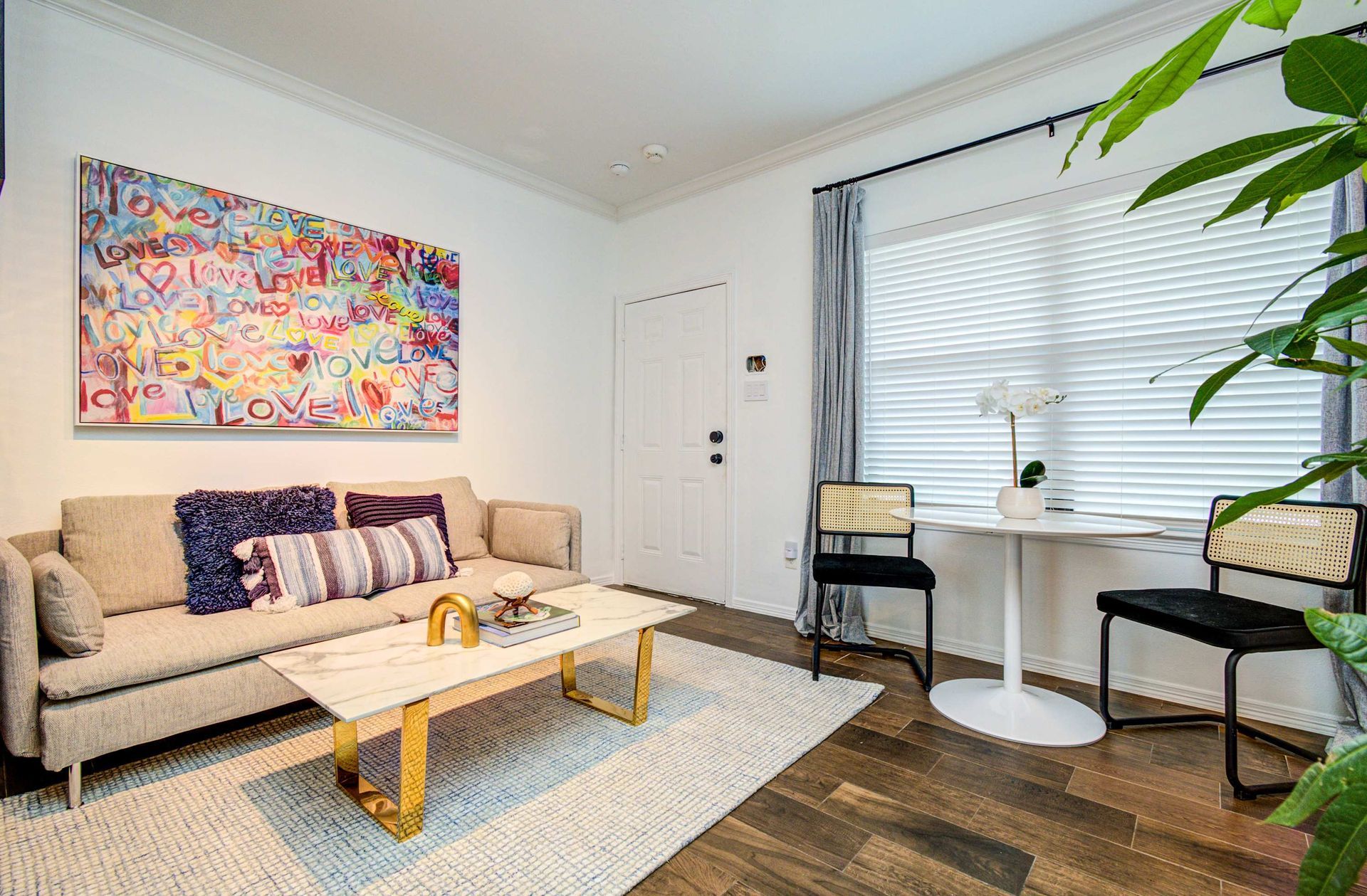 Bright living room with beige sofa, colorful wall art, white coffee table, and window seating by a large window