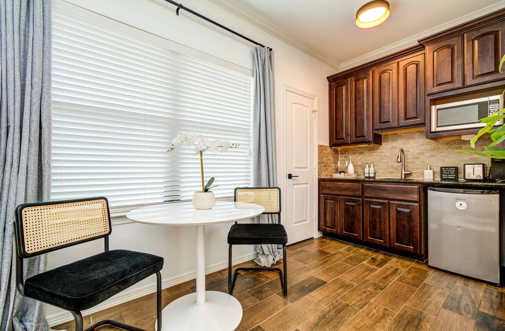 Small kitchen with white table and chairs, dark wood cabinets, stainless appliances, and hardwood floor.