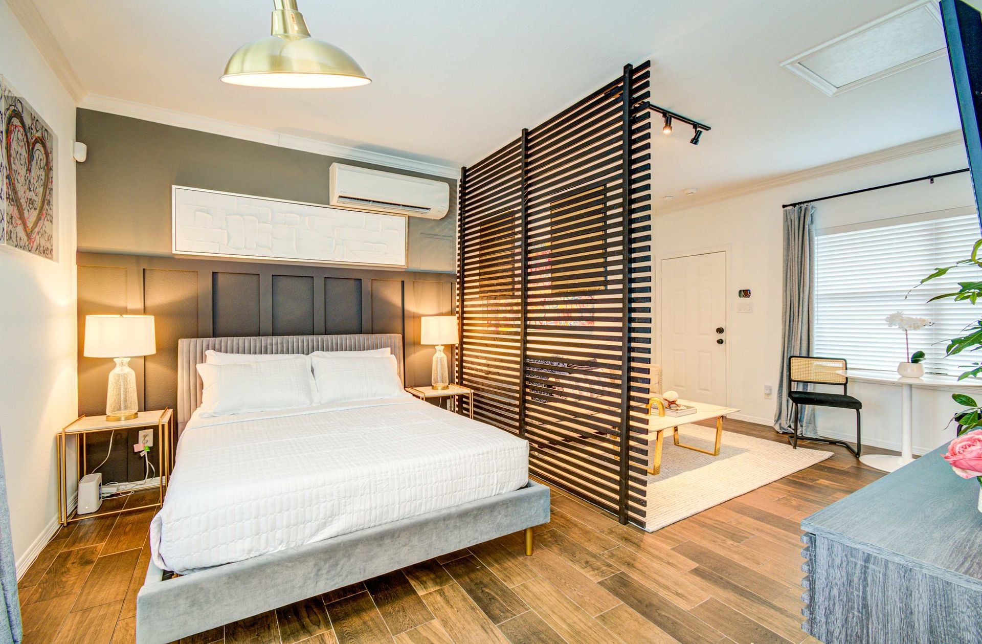 Bright modern bedroom with white bed, wooden floor, black slatted partition, and warm lamp lighting