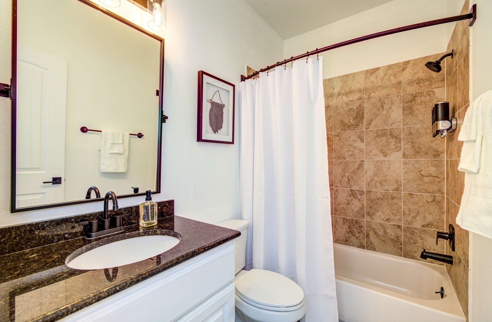 Bathroom with granite vanity, mirror, toilet, and shower with white curtain and tan tile.