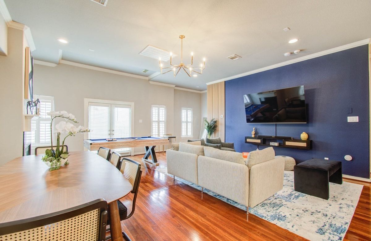 Bright open-concept living room with blue accent wall, wall-mounted TV, beige sofa, and hardwood floors