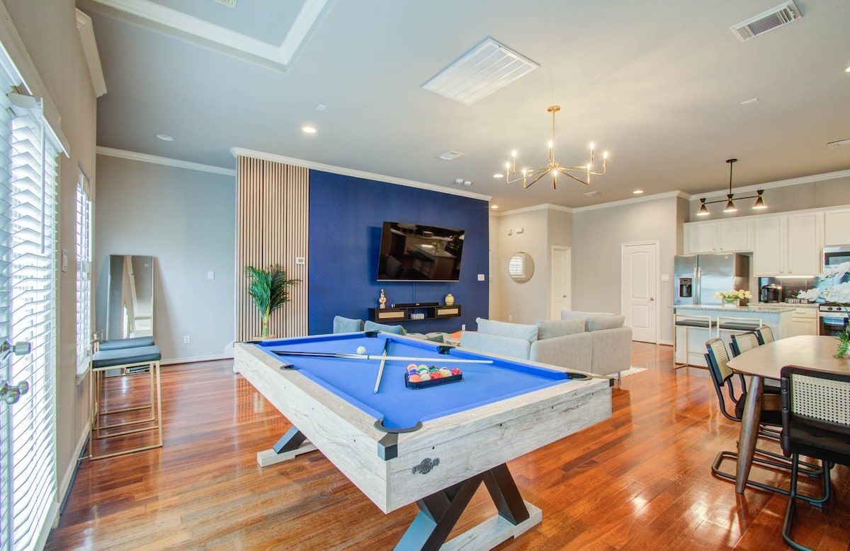 Game room with blue pool table, wall-mounted TV, chandelier, and open kitchen area