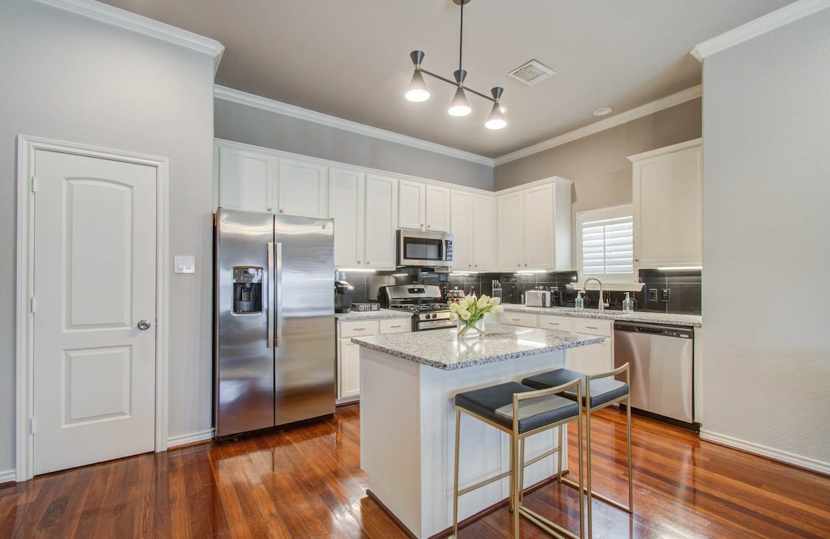 Bright modern kitchen with stainless steel appliances, white cabinets, and a center island on hardwood floors