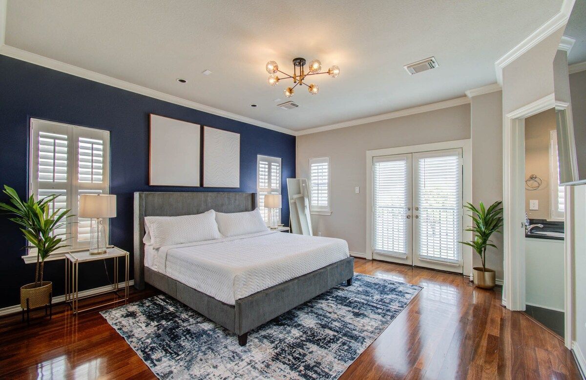 Bright bedroom with a large bed, blue accent wall, white shutters, and a patterned rug.