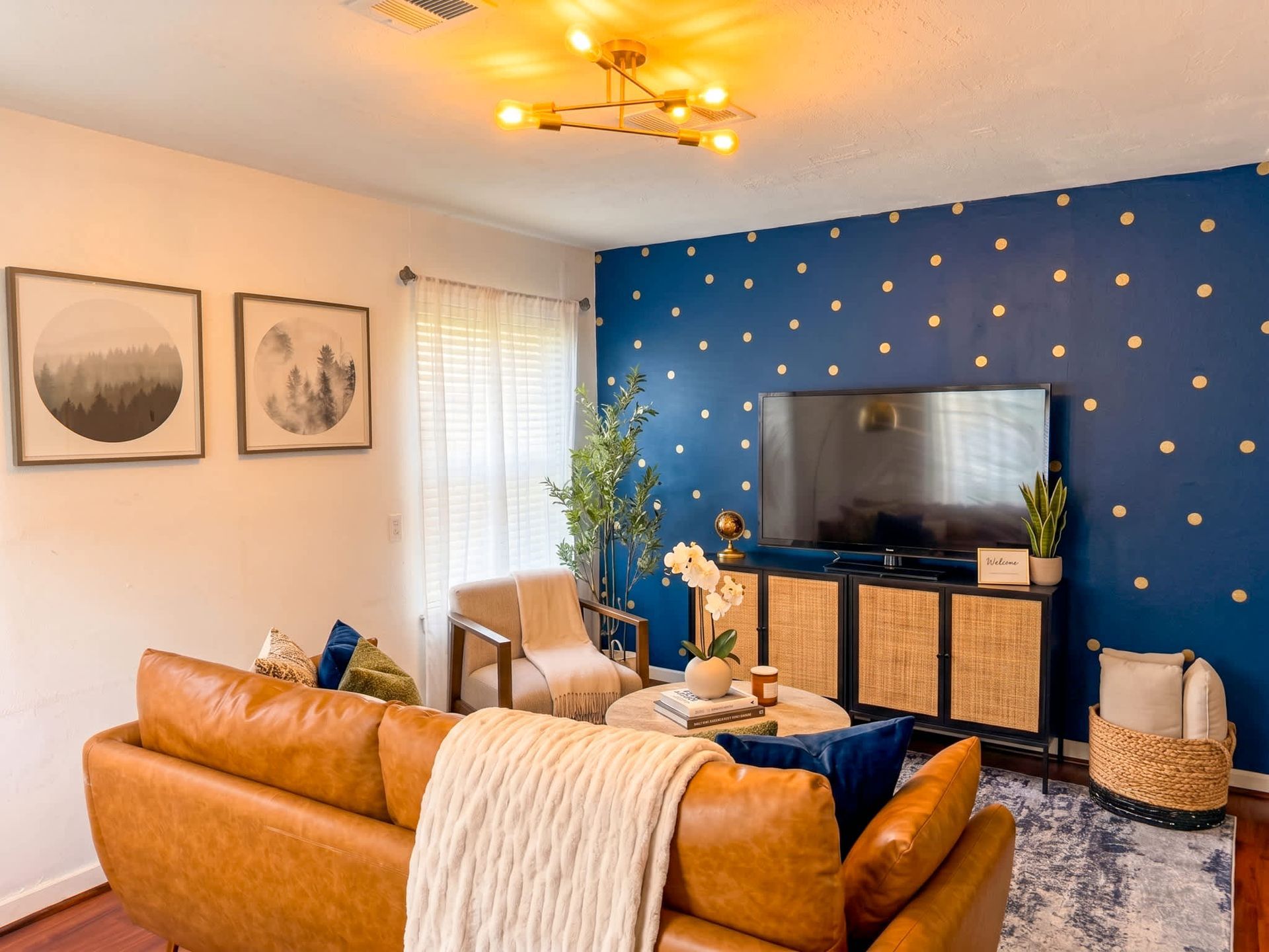 Modern living room with blue accent wall, tan sofa, TV, and warm ceiling light