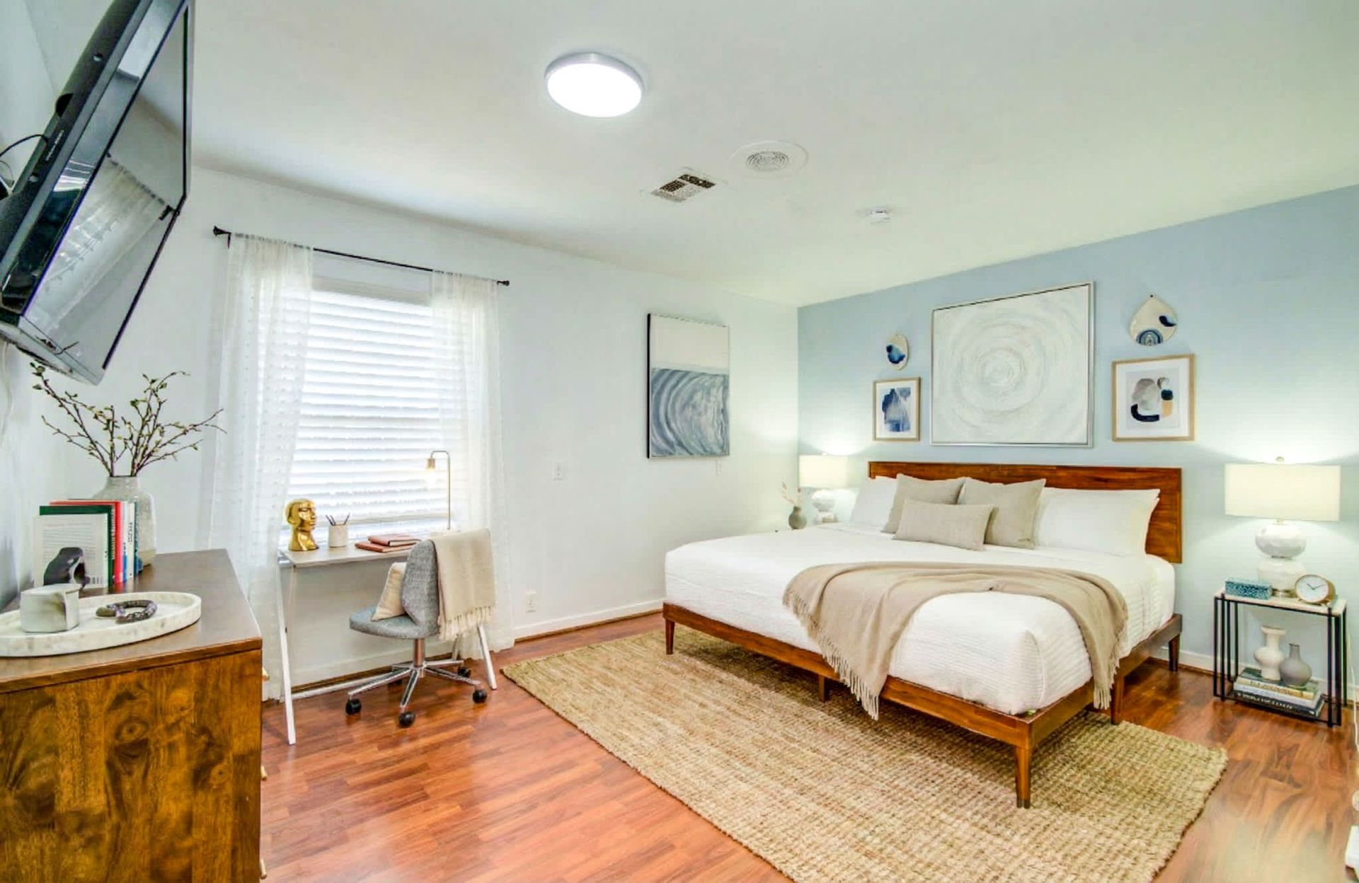 Bright bedroom with a bed, desk, chair, and white walls in a tidy modern apartment