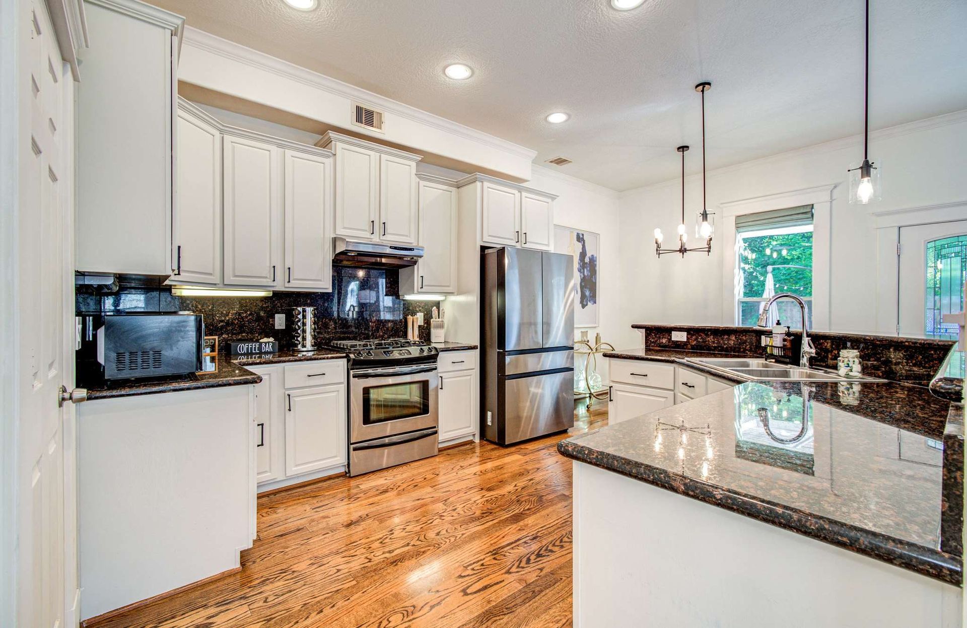 Bright modern kitchen with white cabinets, stainless appliances, granite island, and hardwood floors