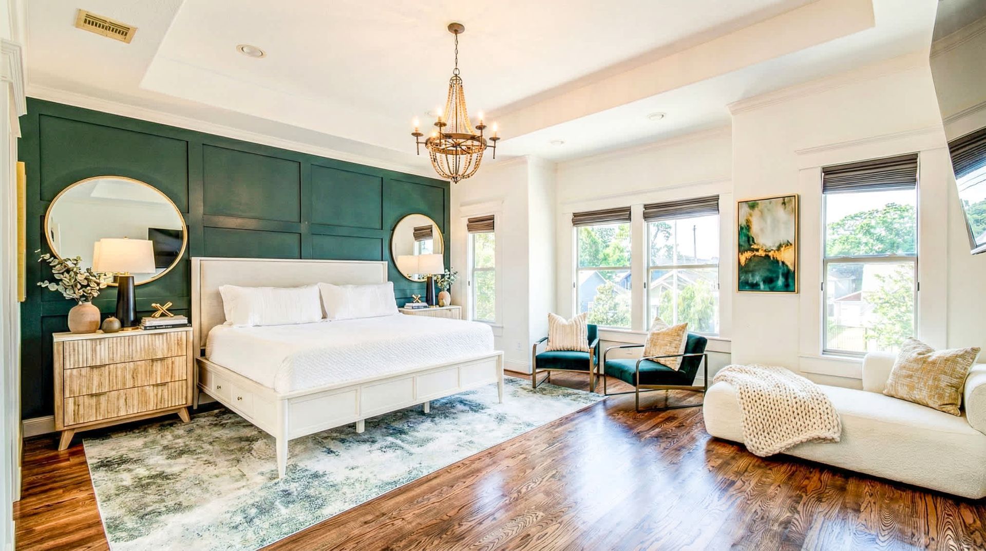 Elegant bedroom with teal accent wall, white bed, chandelier, windows, and hardwood floors