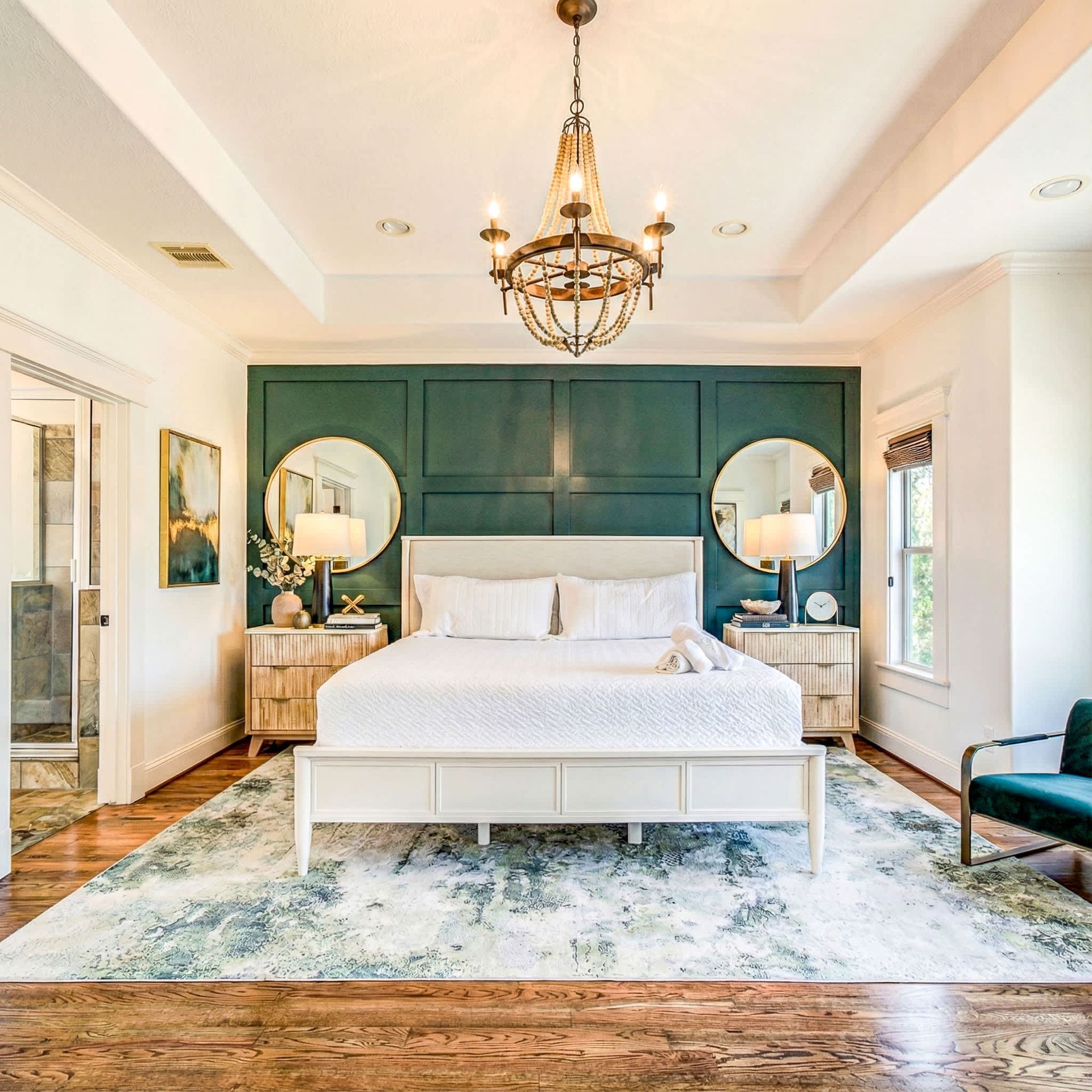 Bright bedroom with green accent wall, white bed, chandeliers, and patterned rug