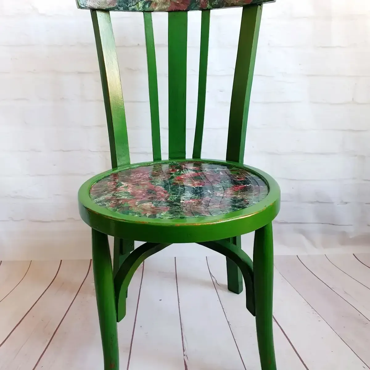 Silla de madera verde con asiento y respaldo estampados contra una pared de ladrillo blanco y piso de madera.