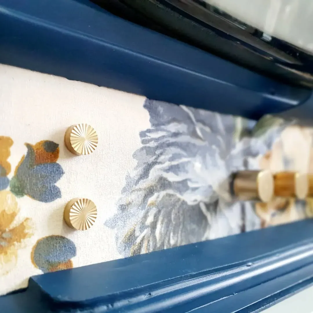 Muebles pintados de azul con papel pintado floral y tiradores dorados.