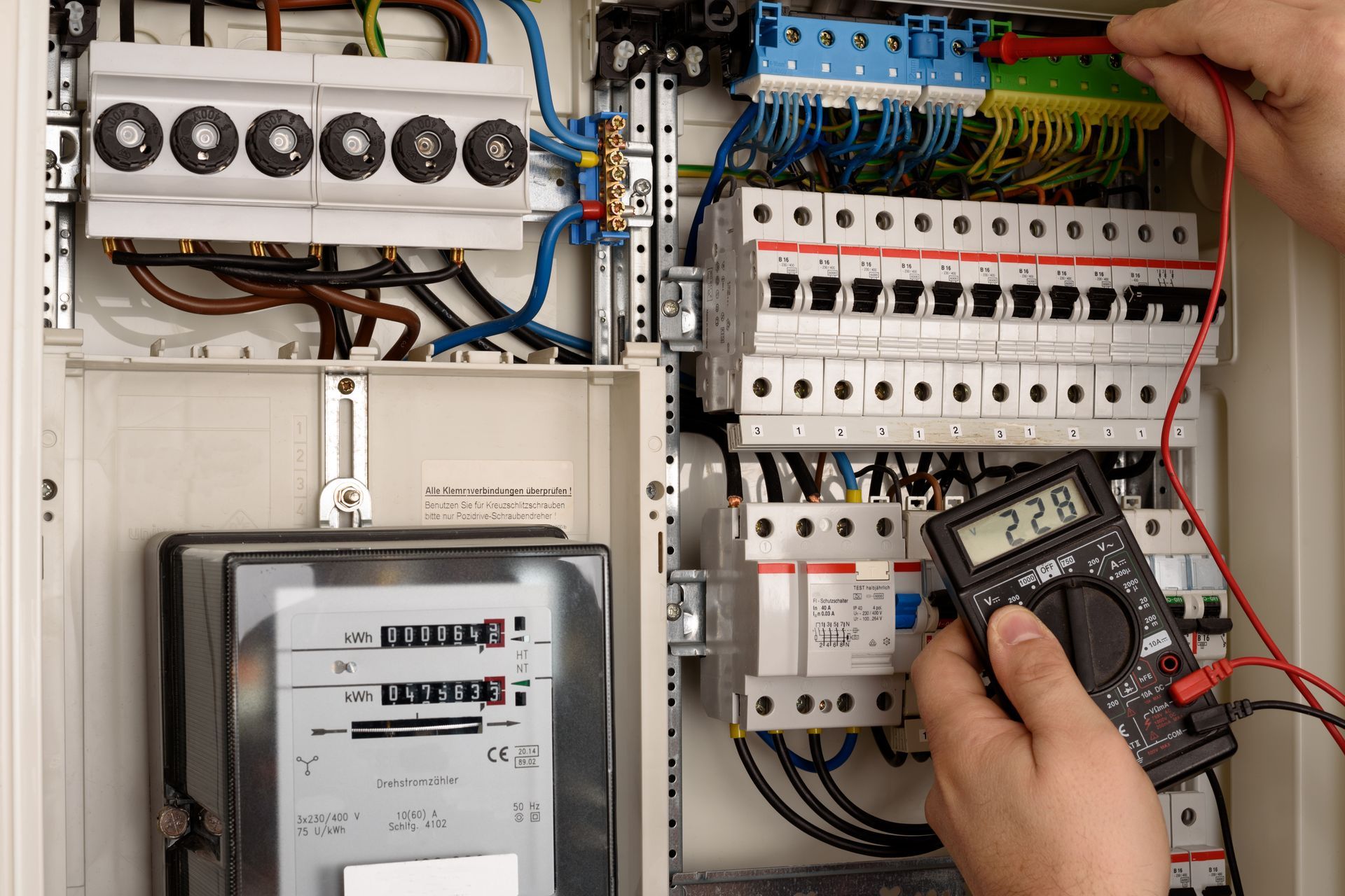 Un électricien teste un tableau électrique avec un multimètre ; les fils et les disjoncteurs sont visibles.