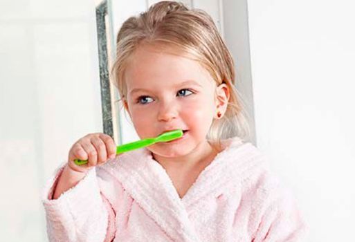 Una niña se cepilla los dientes con un cepillo de dientes verde.