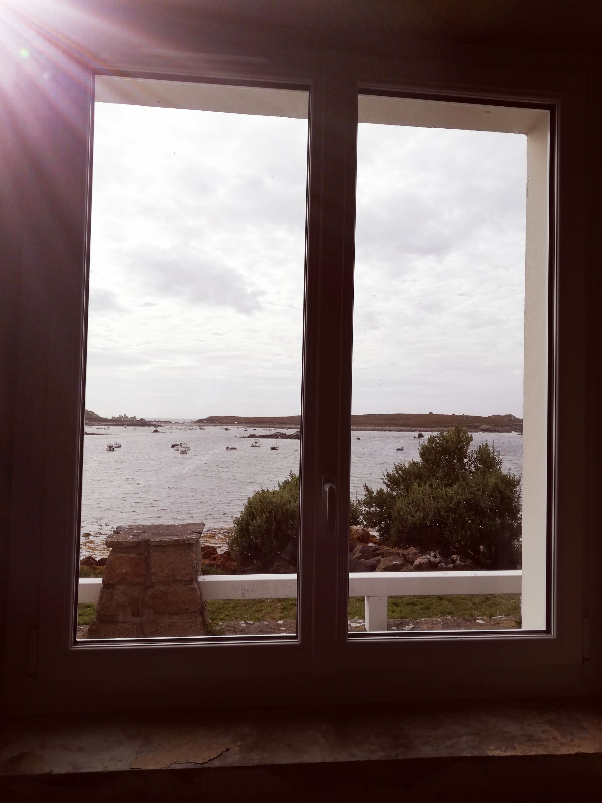 Vue à travers une fenêtre, montrant un ciel nuageux au-dessus d'un plan d'eau et d'une petite île avec de la végétation.