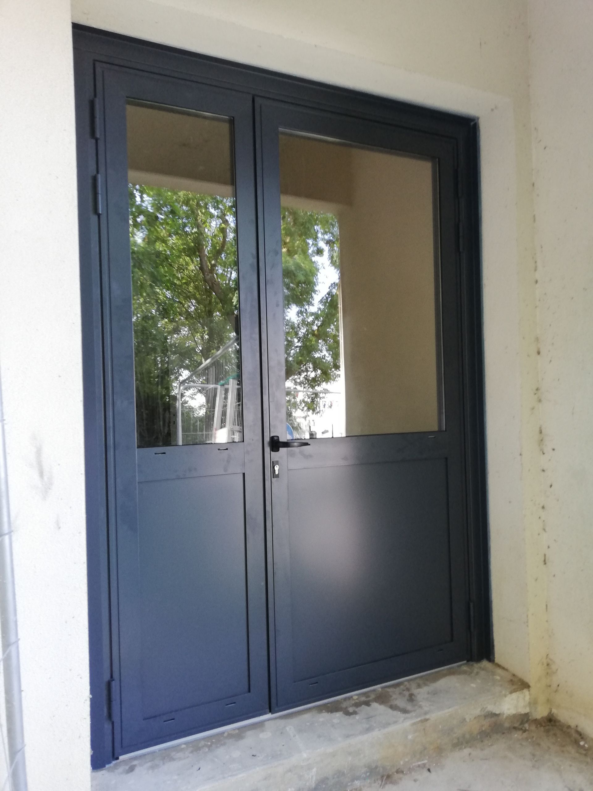 Portes doubles gris foncé avec de grandes vitres; placées dans un mur blanc.