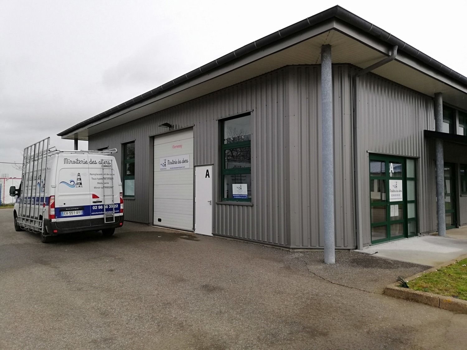 Bâtiment avec une façade en métal gris, une porte de garage fermée et une camionnette bleue et blanche garée.