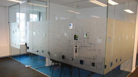 Espace de bureau aux parois de verre avec film de confidentialité dépoli à motifs ; moquette bleue, murs blancs et fenêtre.