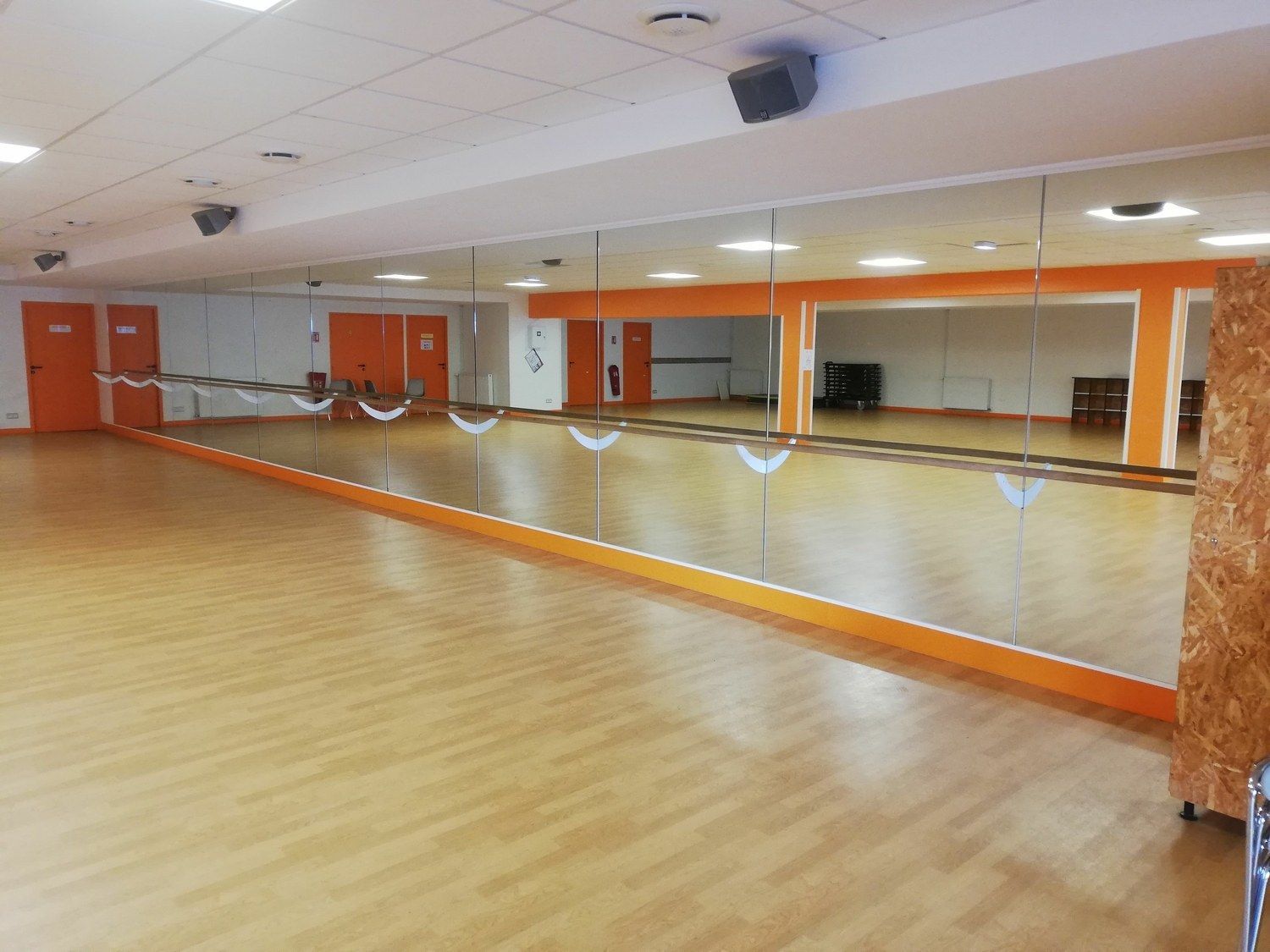 Studio de danse avec plancher en bois, miroirs le long d'un mur, accents orange et haut-parleurs.