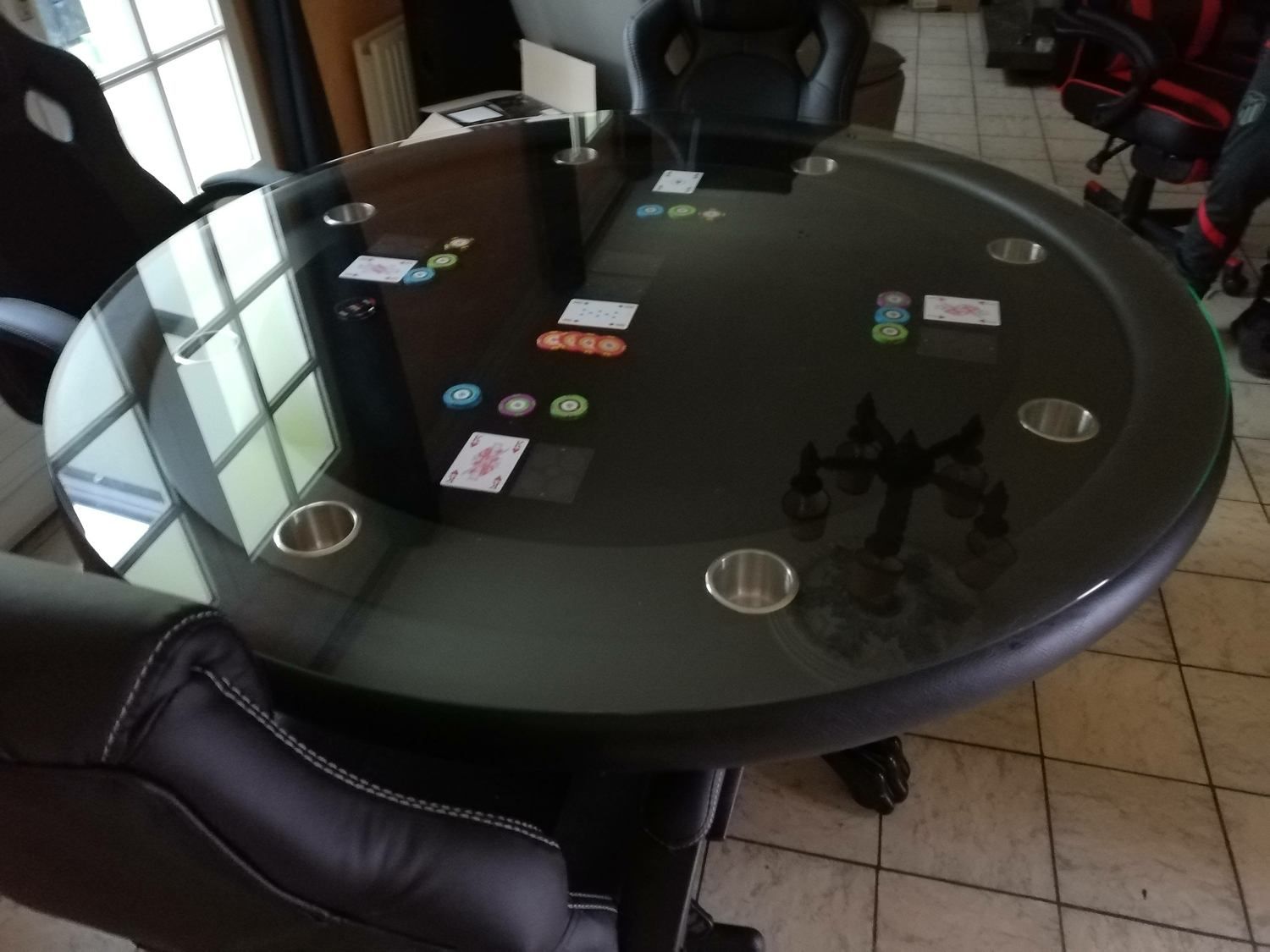 Une table de poker ronde et noire avec des porte-gobelets, des cartes et des jetons intégrés.
